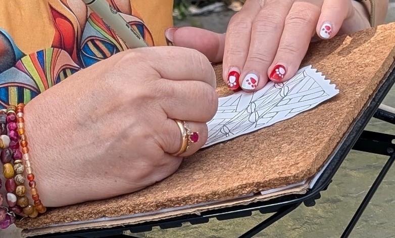 Hands drawing structured Zentangle patterns on a small paper tile